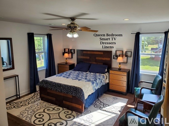 A bedroom with a queen bed, a ceiling fan, and a window with blue curtains.