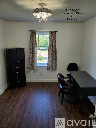 A room with a desk, chair, and cabinet with a window and curtains.