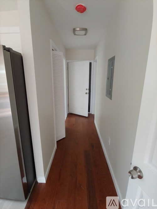 A hallway with a refrigerator on the left and a door on the right.