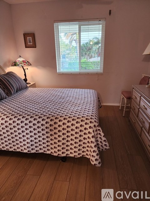 A bedroom with a bed, a nightstand with a lamp, and a window with blinds.