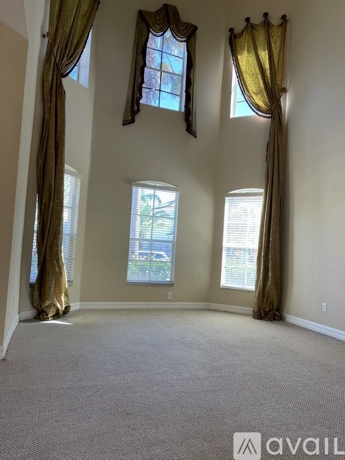 A room with carpeted floor, three windows with curtains, and a logo that reads "AVAIL".