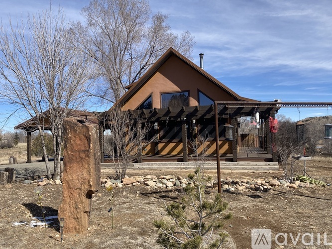 A house with a brown roof and a porch is surrounded by trees and rocks.