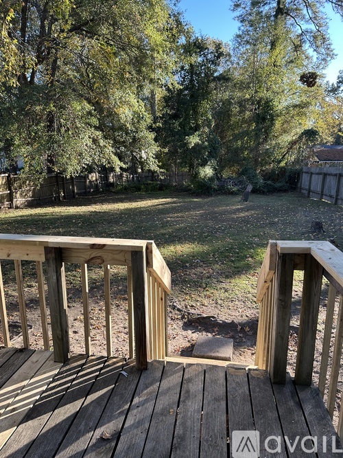 A wooden deck with a railing and steps leading to a grassy area.