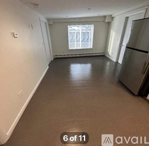 A spacious empty room with a window and a refrigerator in the corner.