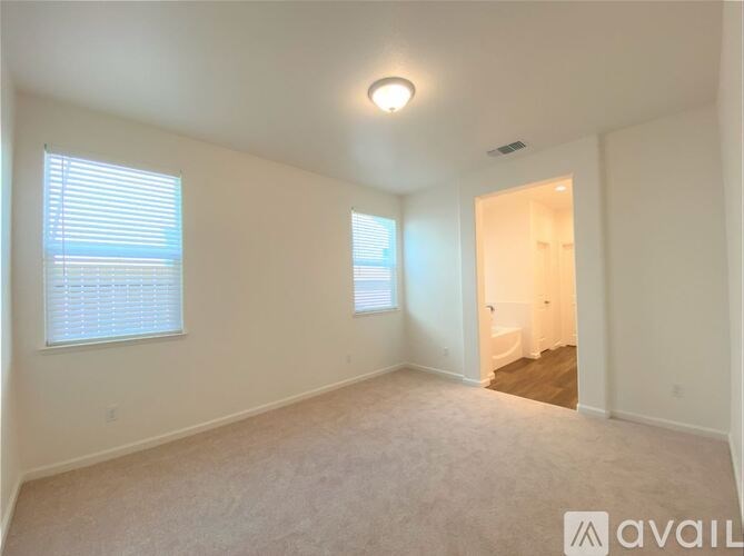 A spacious room with a carpeted floor, a window with blinds, and a door leading to another room.