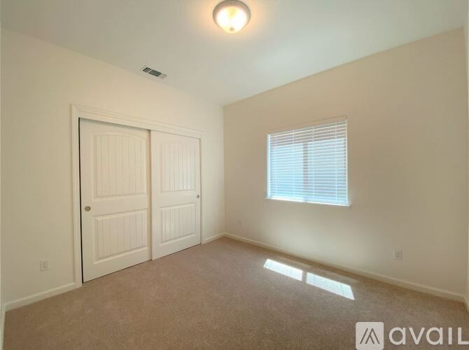 A room with a carpeted floor, a window with blinds, and a door with a window above it.