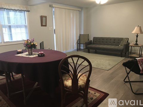 A living room with a grey couch, a round table with a purple tablecloth, and a chair with a wooden design.