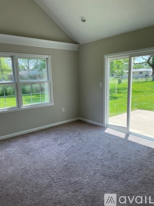 A room with a carpeted floor and a sliding glass door leading to a grassy area.