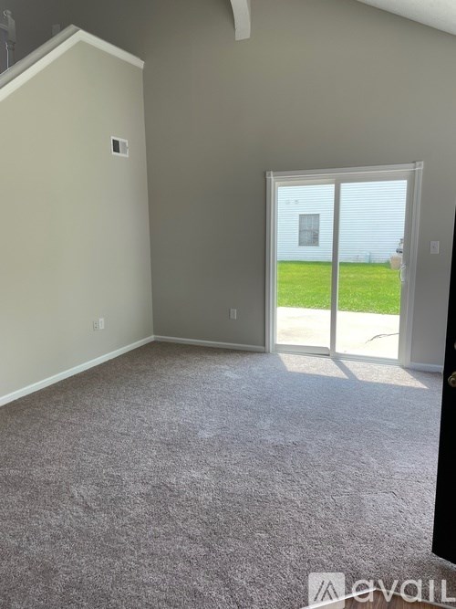A room with a carpeted floor and a sliding glass door leading to a green lawn.