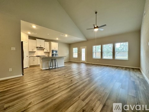 A spacious room with wooden flooring and a kitchen area in the background.