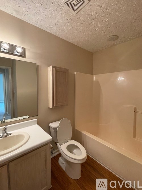 A bathroom with a toilet, sink, mirror, and shower.