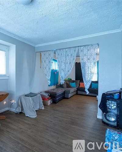 A room with a grey sofa, a grey table, a black speaker, and a white curtain.