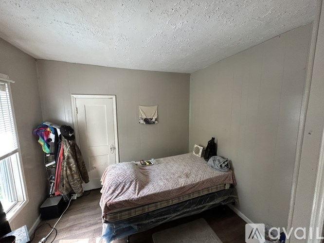 A bedroom with a bed, a window, and a coat rack.