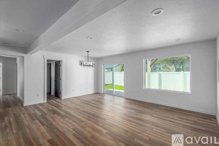 A room with wooden flooring and white walls, with a window showing a green outdoor area.