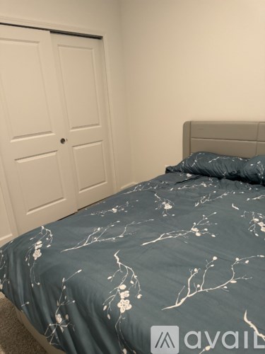 A bed with a grey and white comforter sits in a room with a white door.