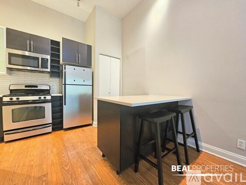 A kitchen with a stove top oven, microwave, refrigerator, and bar stool.