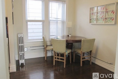 A kitchen with a table and chairs in the foreground and a doorway with a picture on the wall in the background.