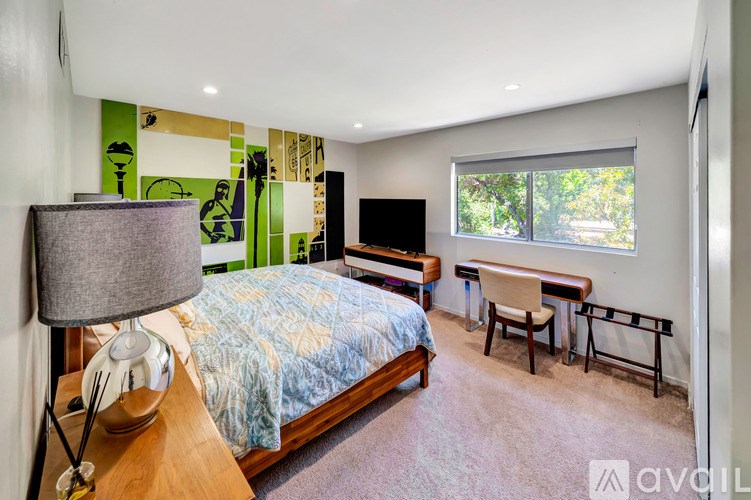 A bedroom with a bed, desk, chair, and lamp.