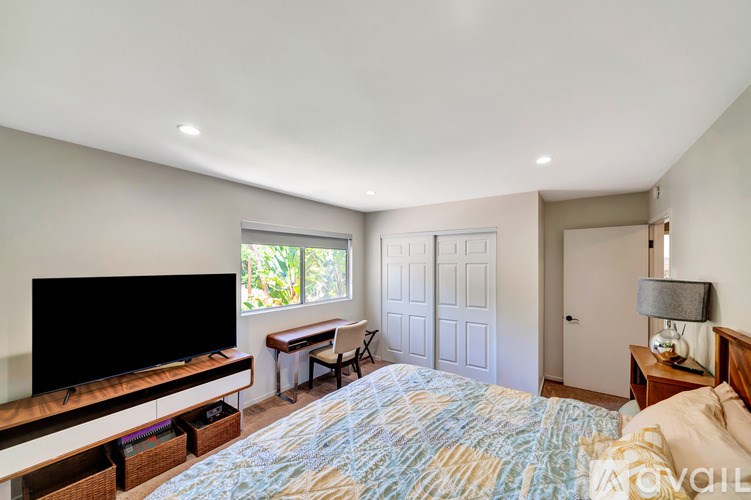 A bedroom with a bed, a desk, and a television.