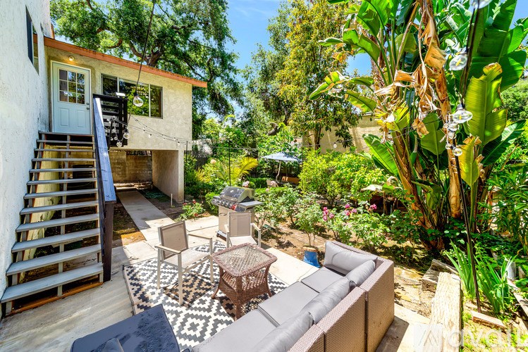 A patio with a couch, chairs, and a table is surrounded by green plants.