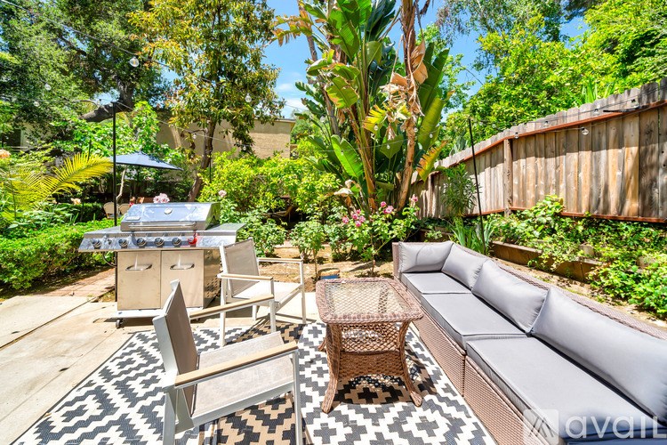 A patio with a grey couch, a wicker table and chairs, and a black and white rug.