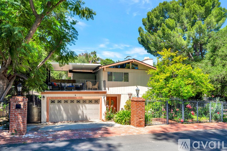 A house with a garage is surrounded by greenery and has a fence around it.