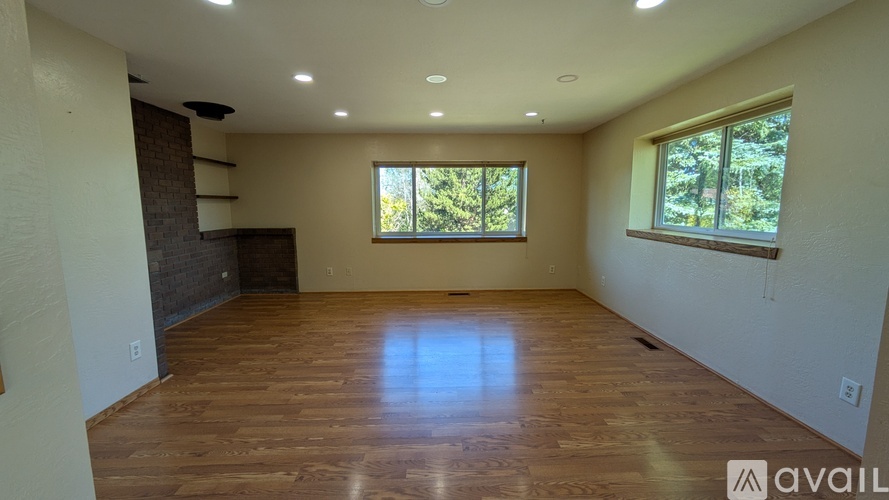 A spacious room with wooden flooring and large windows.