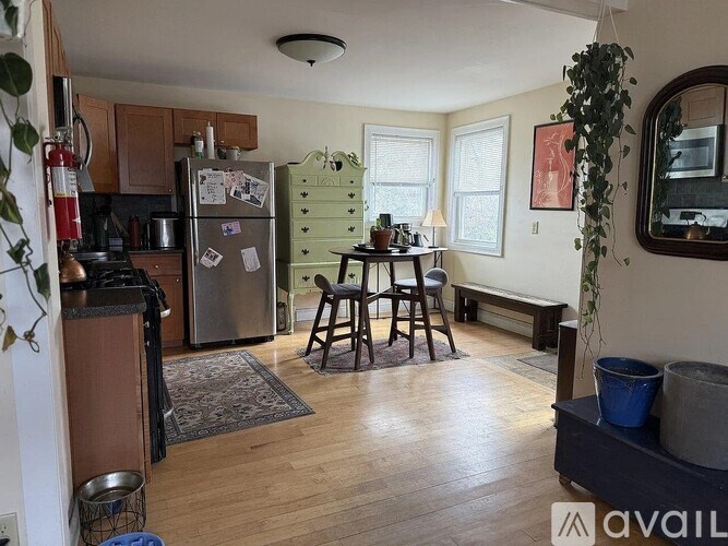A kitchen with a refrigerator, a dining table with chairs, and a potted plant.