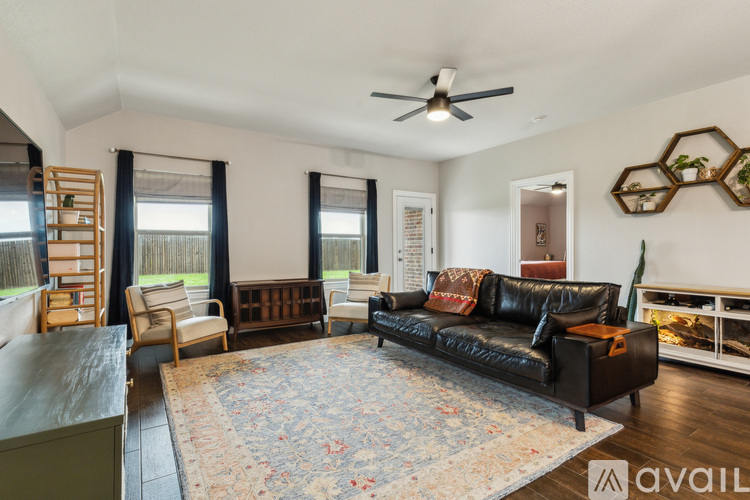 A living room with a black leather couch and a rug.