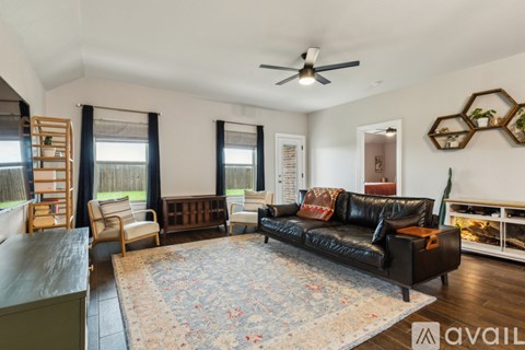 A living room with a black leather couch and a rug.
