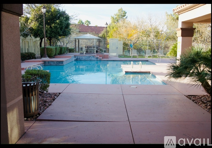 A pool surrounded by a concrete patio and a metal trash can.