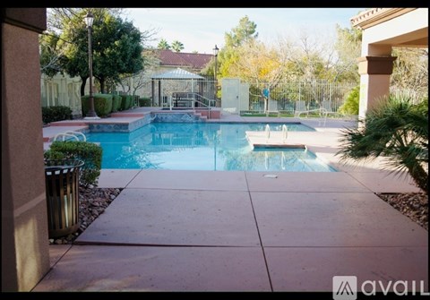 A pool surrounded by a concrete patio and a metal trash can.