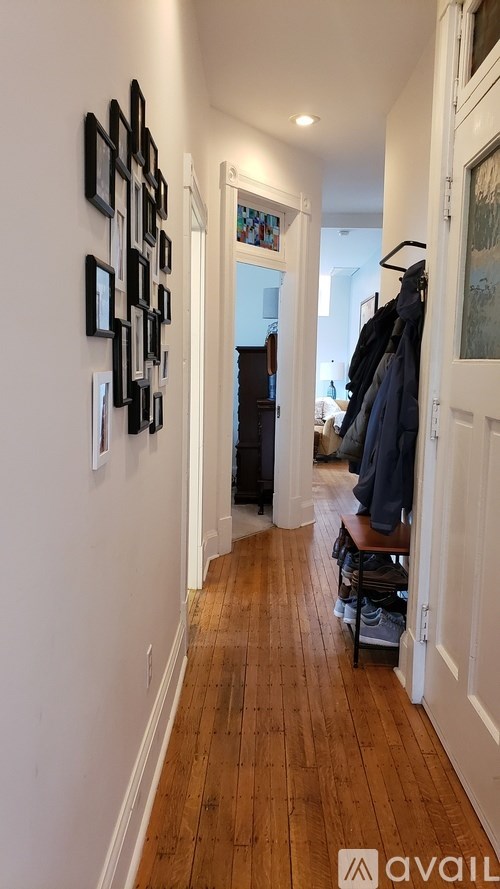 A hallway with a wooden floor and a wall with picture frames on it.
