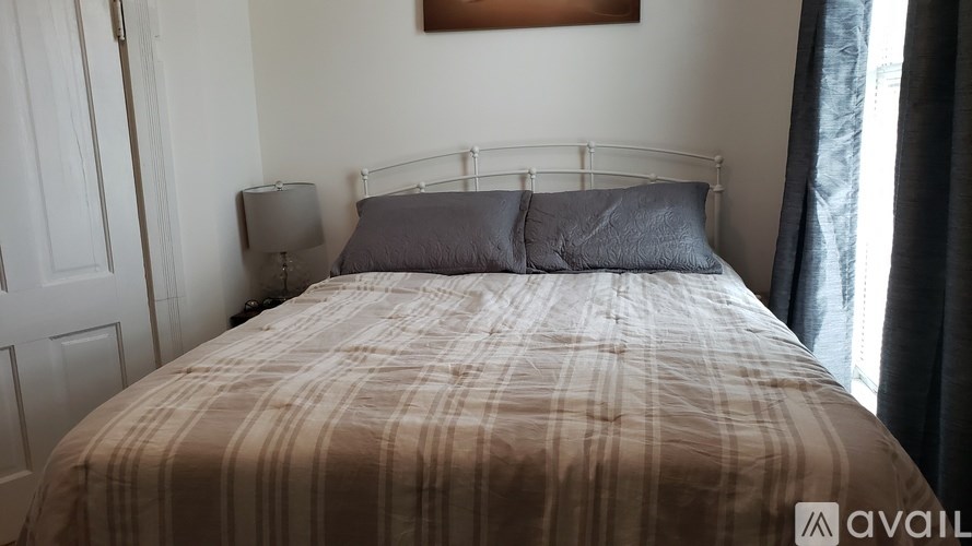 A bed with a striped comforter and two pillows sits in a room with a white door and a window with curtains.