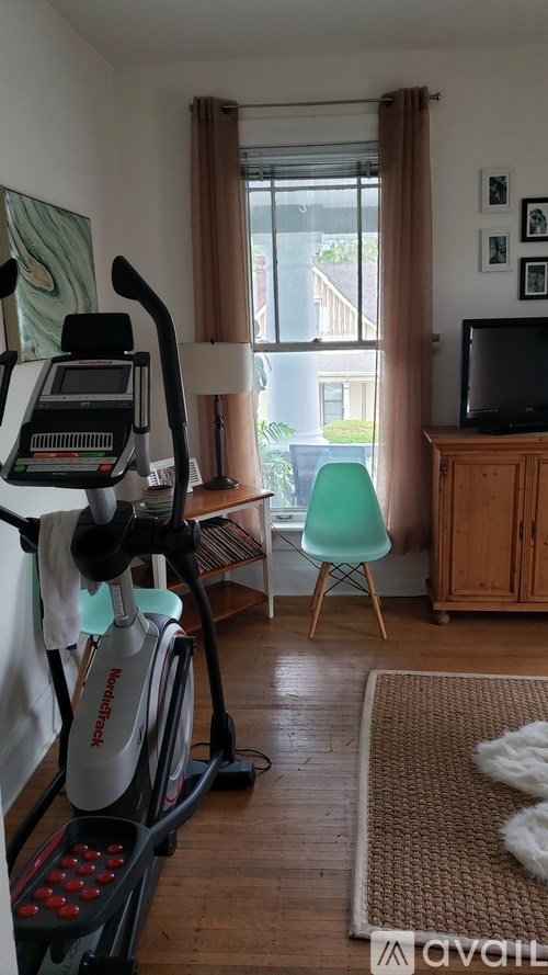 A room with a treadmill, a chair, a television and a window.