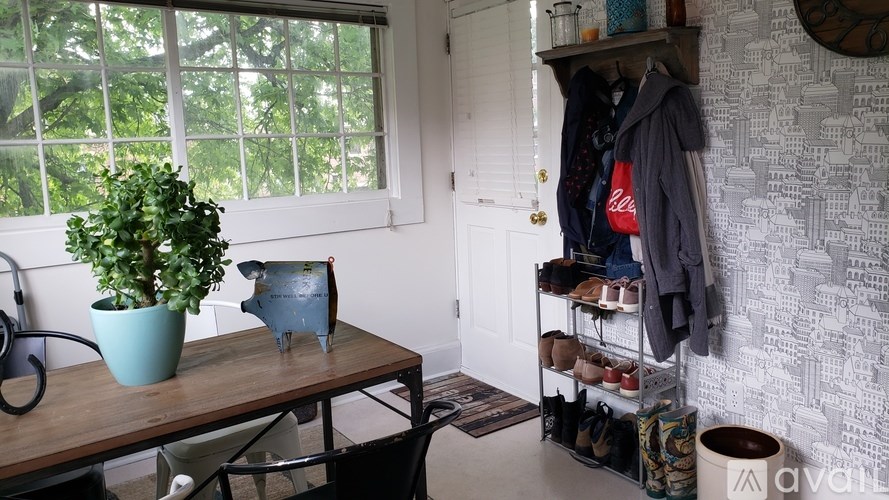 A room with a table, chair, potted plant, and a wall with a clock.