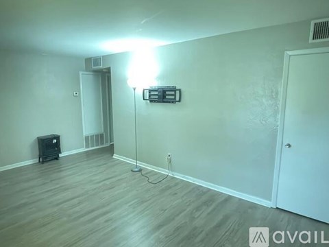 A room with a wooden floor and a white wall with a TV mounted on it.