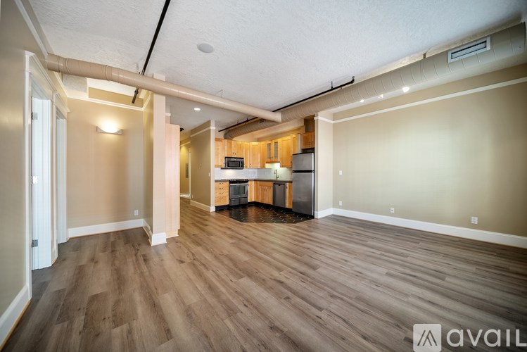 A spacious room with wooden flooring and a kitchen area in the background.
