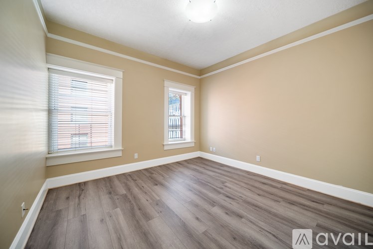 A room with wooden flooring and two windows.