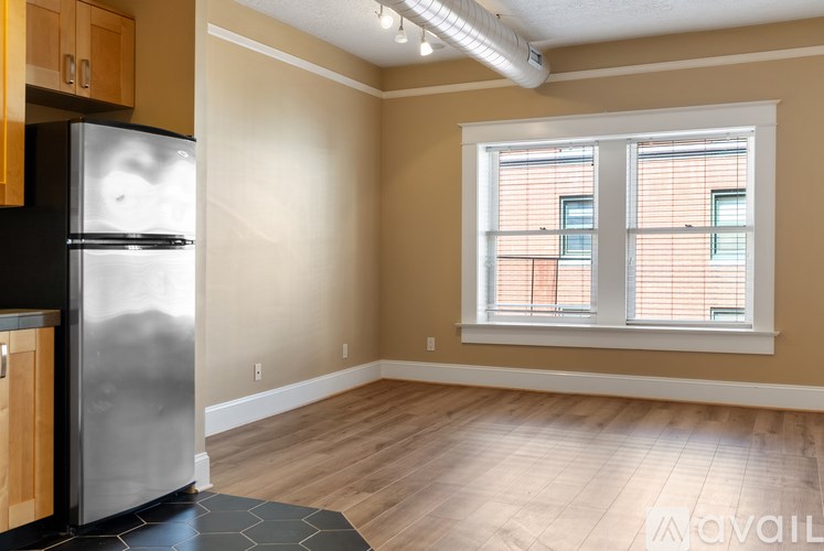 A kitchen with a refrigerator, wooden cabinets, and a window with blinds.
