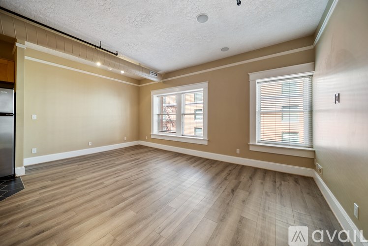 A spacious room with wooden flooring and two windows.
