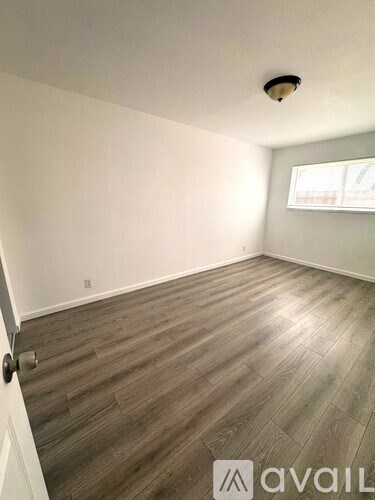 A room with wooden flooring and a door on the left side.