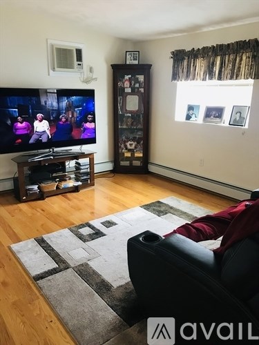 A person is sitting on a black couch in a living room with a television and a cabinet.