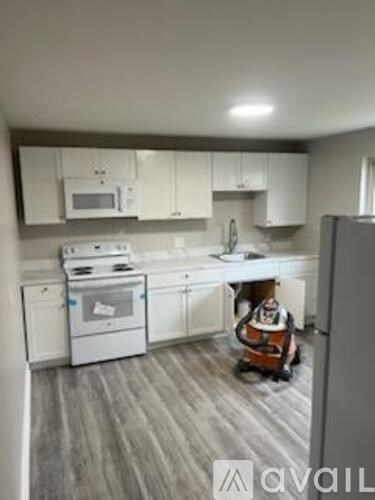 A clean, white kitchen with wood flooring and a refrigerator on the right.