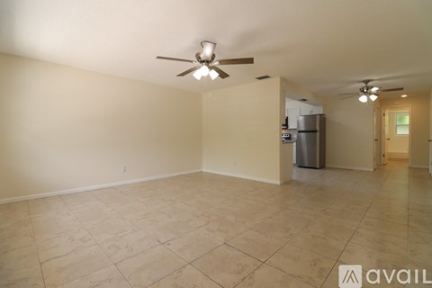 A room with a ceiling fan and a kitchenette in the corner.