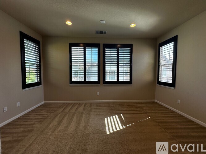 A room with beige walls, carpet, and three windows with blinds.