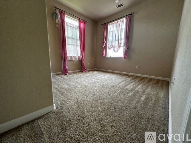 A room with a carpeted floor and two windows with curtains.