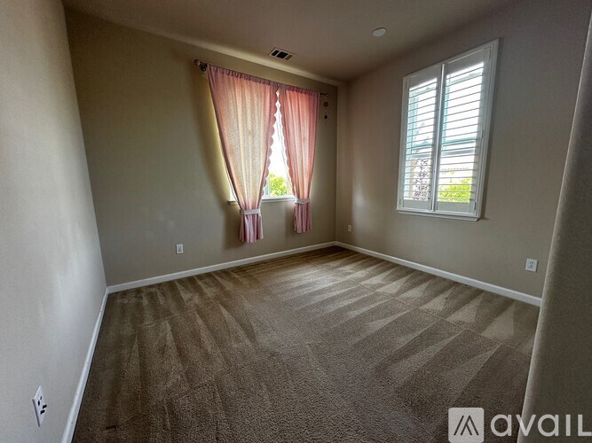 A room with a carpeted floor and a window with pink curtains.