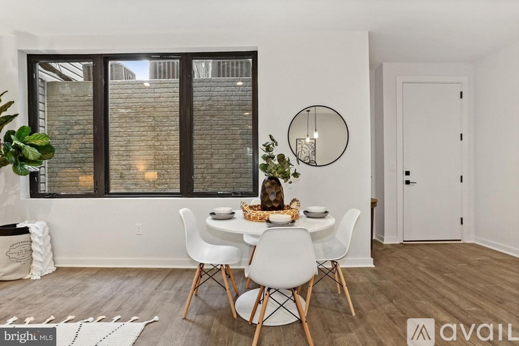A dining room with a white table and chairs, a round mirror, and a plant on the windowsill.