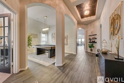 A spacious living room with a pool table and a view of the back of the room through an archway.